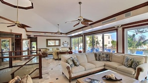 A spacious lobby with a large beige sofa, wooden coffee table, and a glass railing. There are ceiling fans, large windows with a view of palm trees, and a sign indicating an exit. - Brand New Listing!  Beautiful - Upscale newly remodeled Modern Tropical Oasis! (Key Largo)