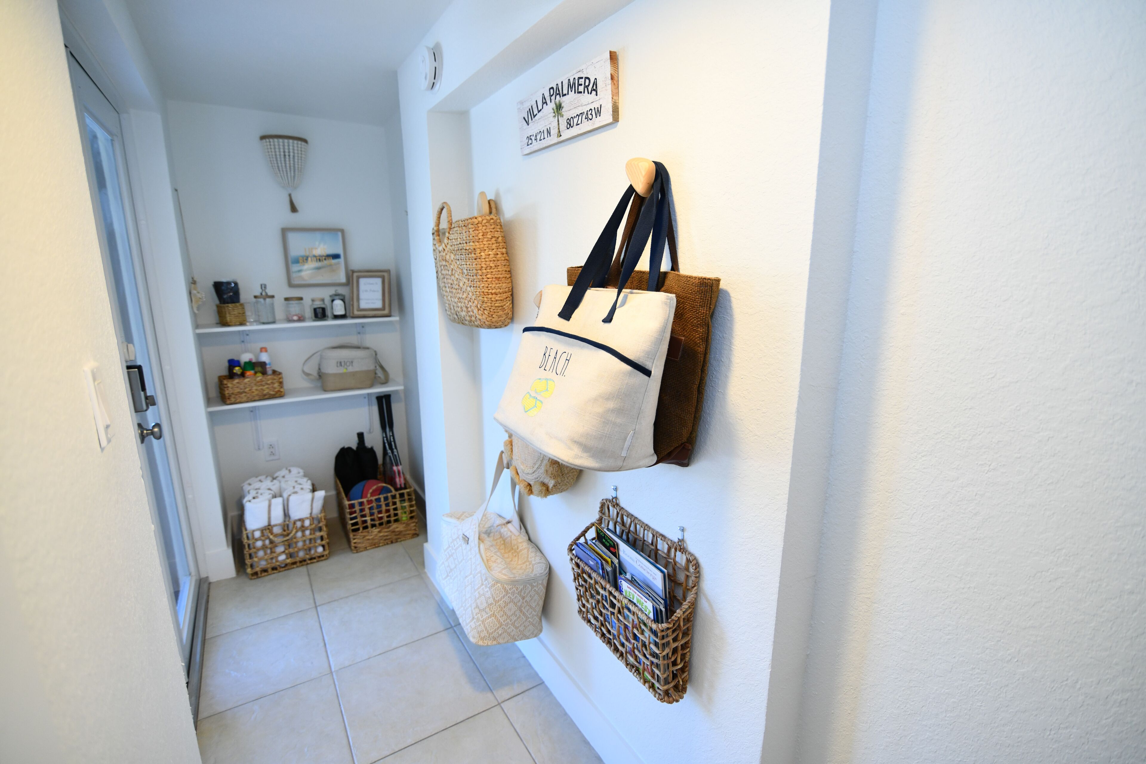 A hallway with a white wall, a sign reading 'Villa Palmera,' and various bags and baskets.