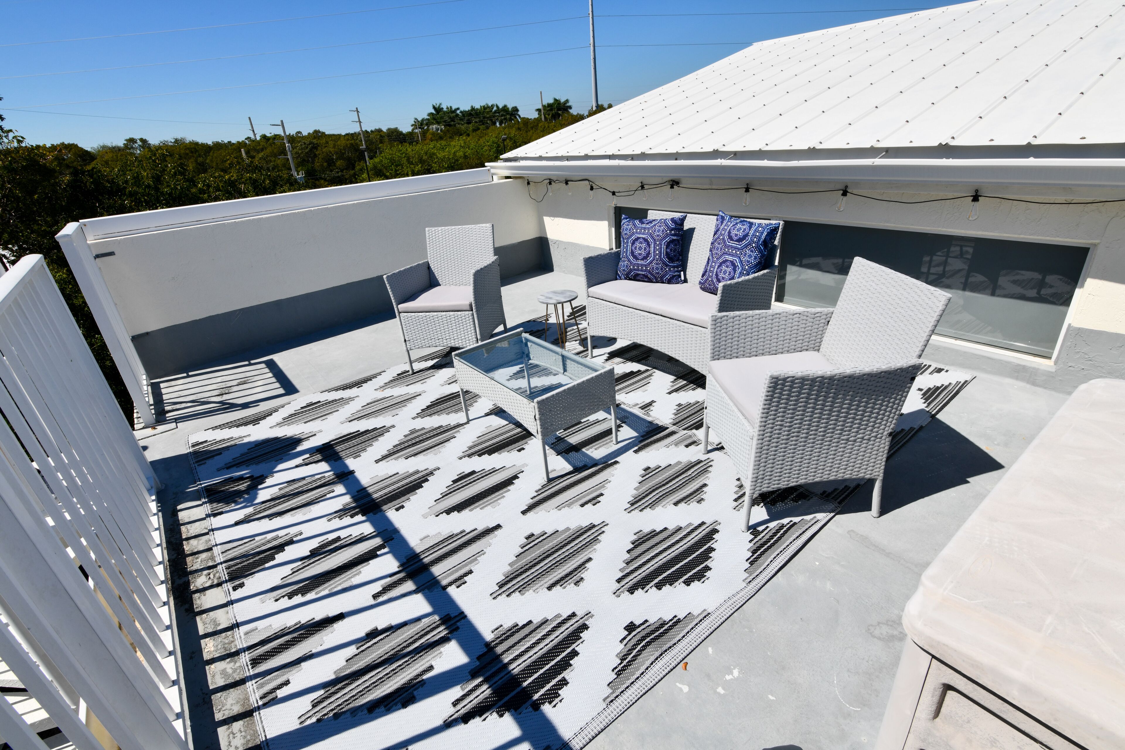 Een terras op het dak met buitenmeubilair, een glazen tafel en een gebouw met een wit gevel en een gedessineerd dak.