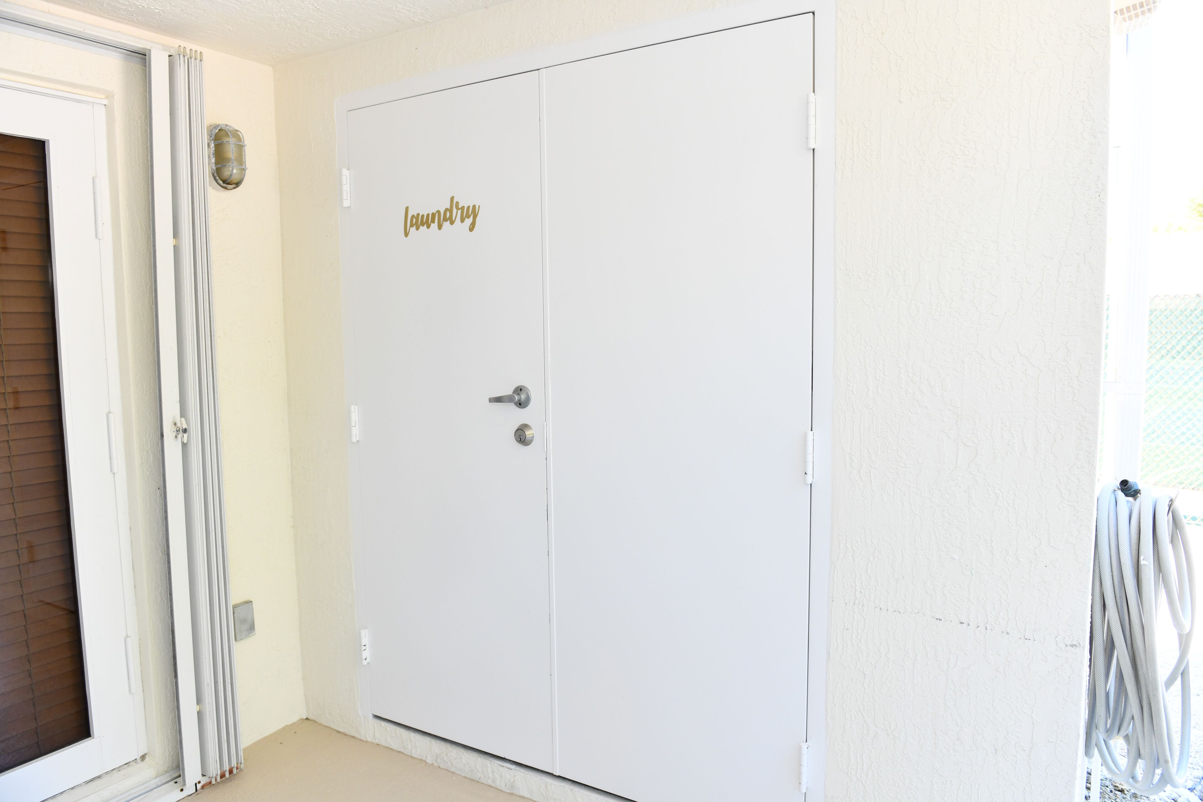 Een witte deur met een gouden bordje met de tekst 'laundry', een schuifdeur van glas, en een witte muur met een lamp.