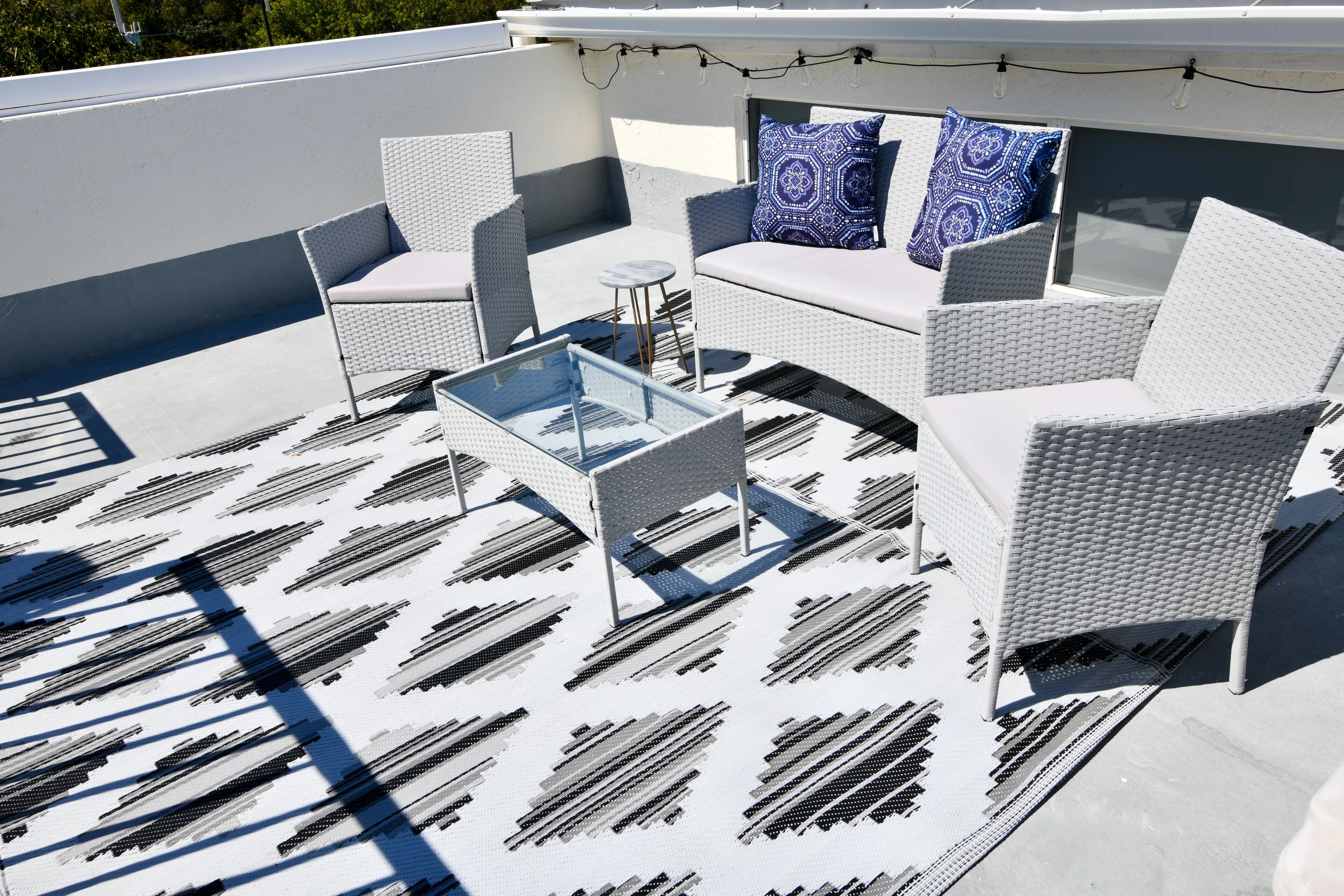 A rooftop terrace with white wicker furniture, a glass coffee table, and patterned rugs.