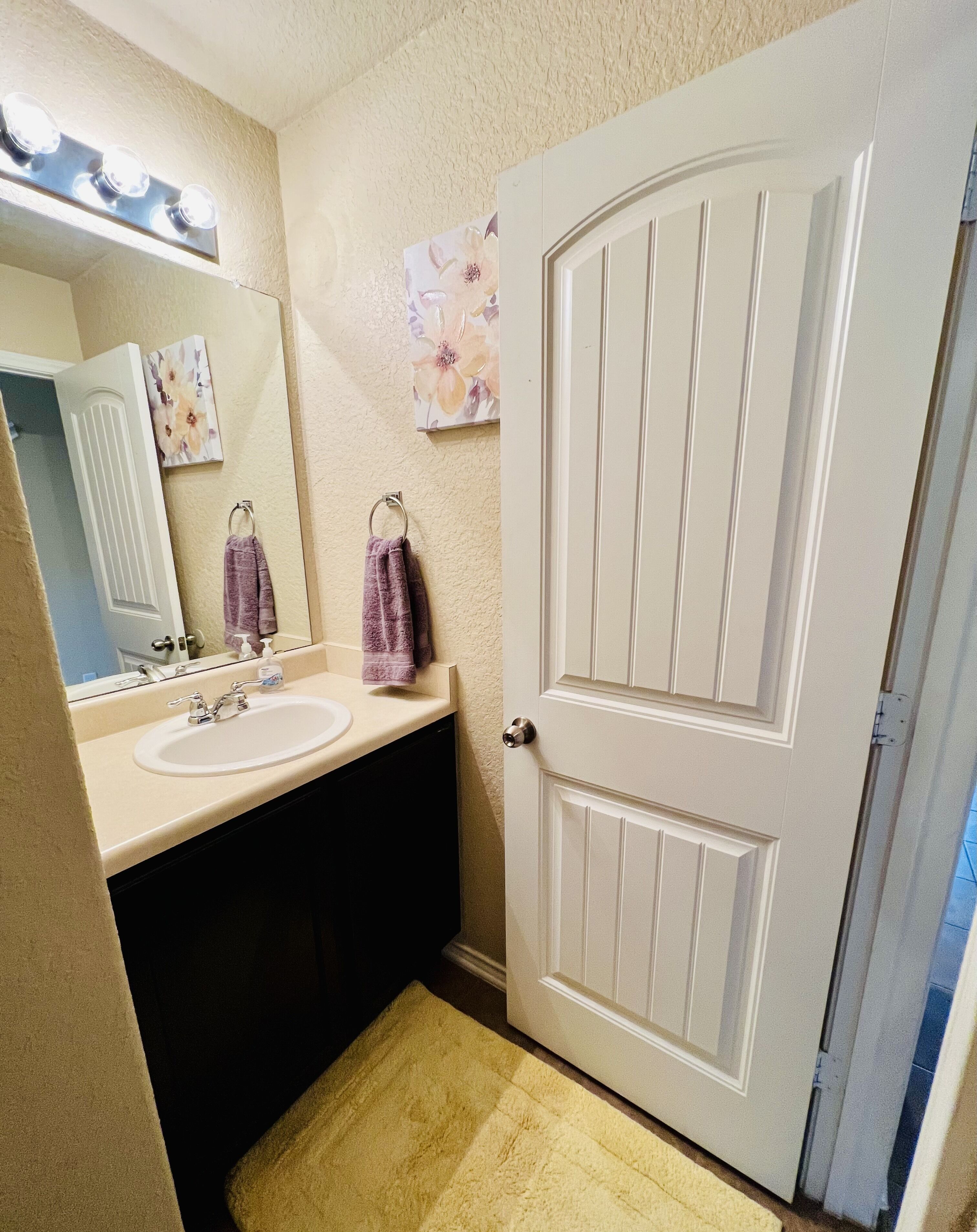 Une salle de bain avec deux lavabos, un miroir, une porte et un luminaire placé au-dessus du miroir.