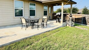 Une terrasse couverte avec une table et des chaises, un barbecue et une clôture en bois.