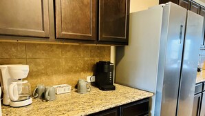 Une cuisine avec des meubles de rangement en bois foncé, un réfrigérateur en acier inoxydable, une machine à café et un plan de travail en granit.