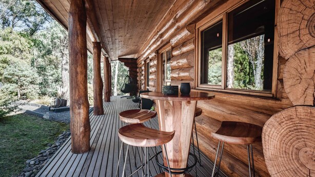 A wooden deck with a wooden table and bar stools, surrounded by trees. - Cuan Den Log Cabin - Base Of Mt Buller - Book Now For School Holidays! (Sawmill Settlement)