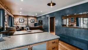 A modern log cabin interior with a stone countertop, wooden furniture, and a large window offering a view of the outdoors. - Cuan Den Log Cabin - Base Of Mt Buller - Book Now For School Holidays! (Sawmill Settlement)