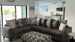 Uma sala de estar moderna com um sofá modular cinza, um banquinho estampado e um ventilador de teto.