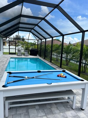 A covered outdoor pool area with a pool table and pool cues. - Brand New Construction Heated Salt Water Pool Home, Paradise in Cape Coral!!! 🌴  (Cape Coral)