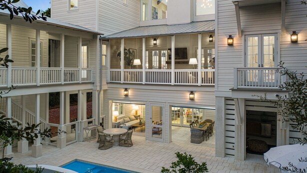 Ein mehrgeschossiges Haus mit überdachter Terrasse, Sitzgelegenheiten im Freien und einem Swimmingpool.