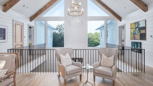 Ein geräumiges Zimmer mit hohen Decken, einer Kristallleuchtre, zwei Sesseln, einem kleinen Tisch und einem Balkon mit Geländer.