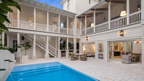 Ein zweistöckiges Haus mit Swimmingpool, Außenbereich mit Sitzgelegenheiten und überdachter Terrasse.
