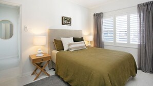 A bedroom with a bed, bedside lamps, a ceiling fan, a window with curtains, and a small bedside table.