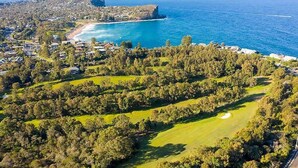 An aerial view of a coastal area with a golf course, residential buildings, and a beach.