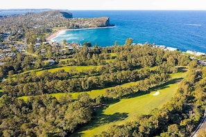 Vista aérea de una zona costera con un campo de golf, edificios residenciales y una playa.