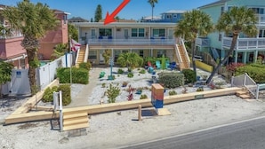 Un motel con edificio central, zona de estar cubierta al aire libre y suelo arenoso.