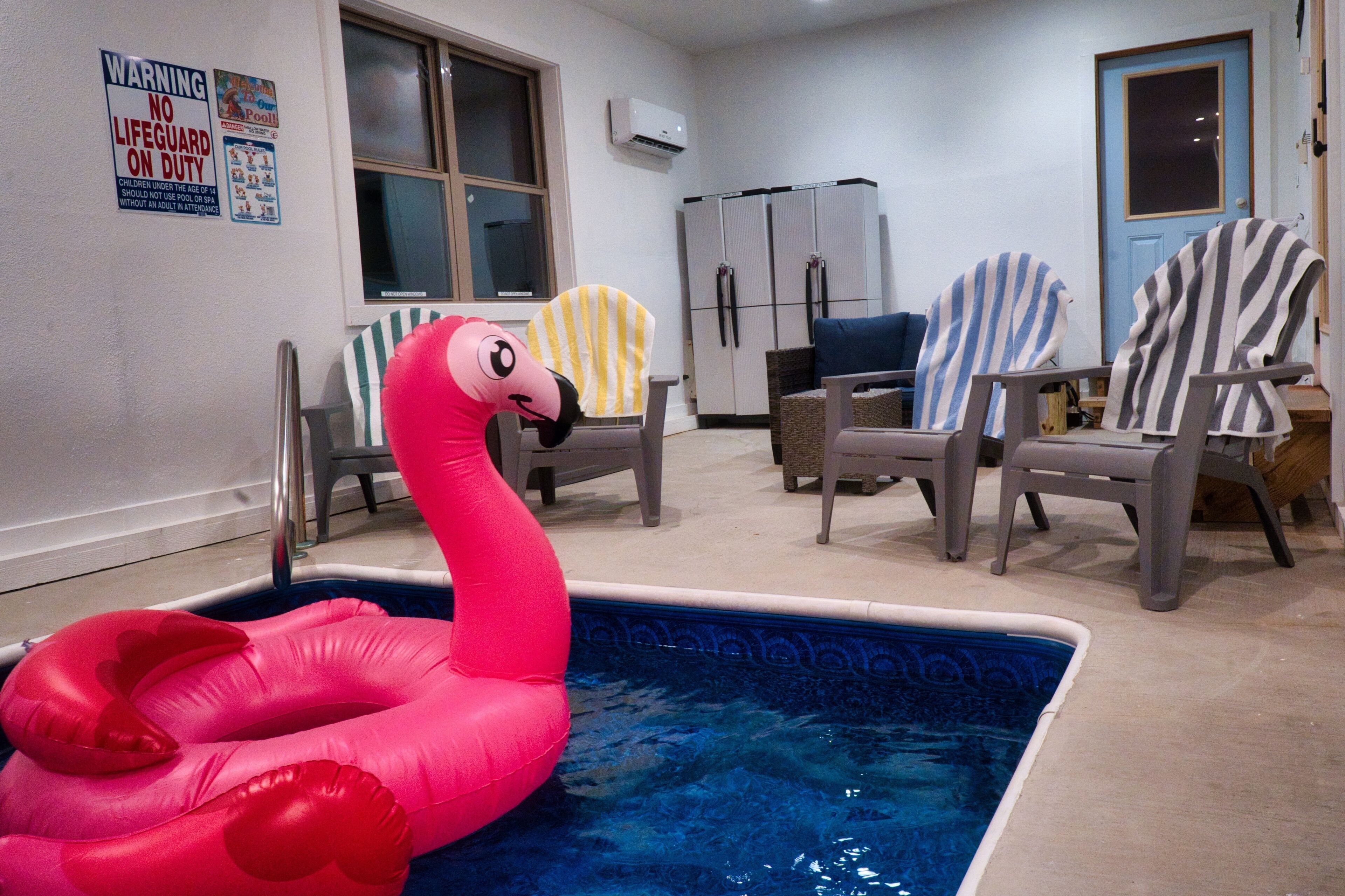 Una piscina con juguetes de flamenco inflables, un refrigerador y sillas a rayas.