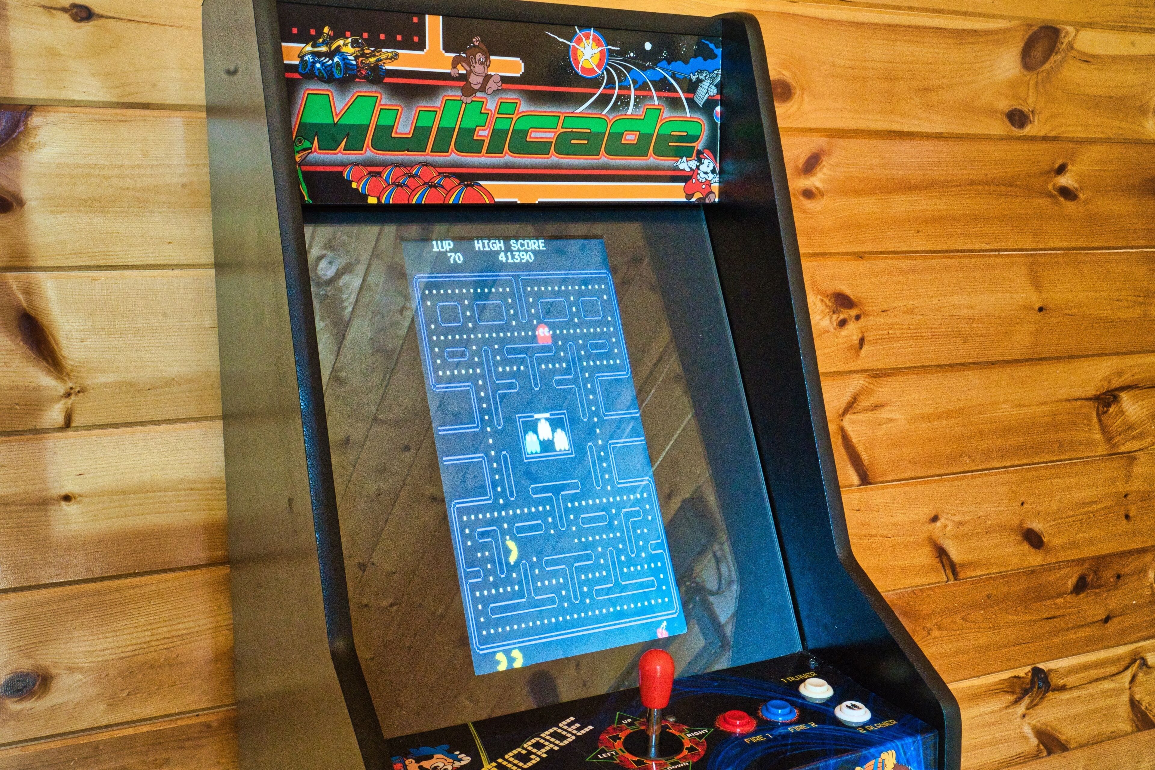 Une borne d’arcade Multicade dotée d’un joystick et de boutons, placée devant un mur en bois.