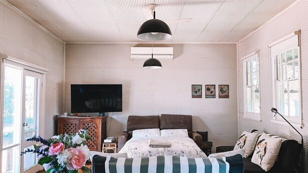 Un dormitorio con una cama, televisión, ventana y un jarrón de flores.