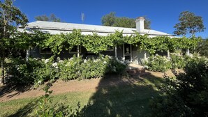 Una casa con un porche cubierto, una chimenea y un jardín con plantas blancas en flor.