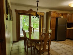 Une cuisine avec des meubles en bois, un réfrigérateur en acier inoxydable, une table à manger avec des chaises et un lustre.