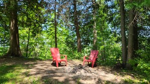 Deux chaises rouges dans une clairière au cœur d’une forêt, avec des arbres et la lumière du soleil.