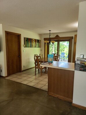 Un coin repas avec une table et des chaises en bois, un lustre et une vue sur l’extérieur grâce à une grande fenêtre.