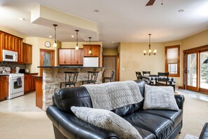 A modern kitchen with wooden cabinets, a stone island, and a dining area with a black leather couch.