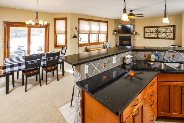 A kitchen with a black countertop, wooden cabinets, a dining area with a checkered tablecloth, and a fireplace.