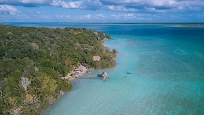 An aerial view of a tropical island with clear turquoise waters, dense green vegetation, and a small settlement with thatched-roof structures.