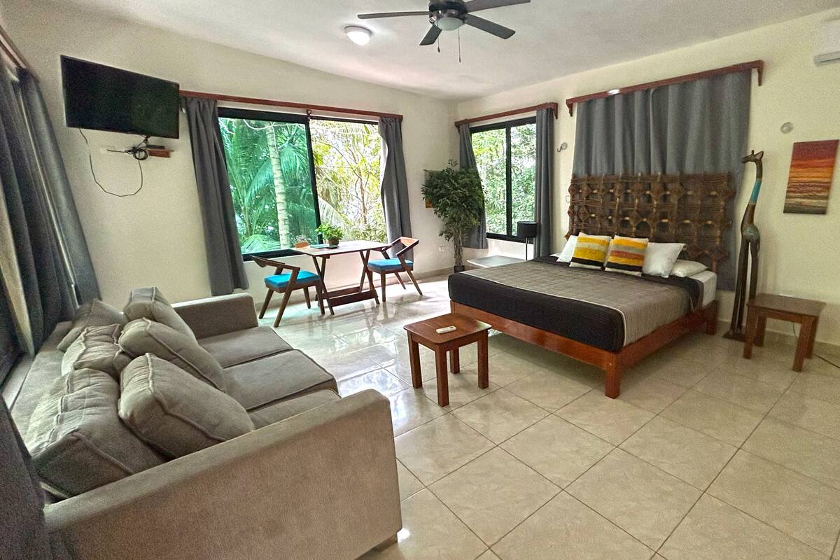 Habitación de hotel con cama, sofá, mesa de comedor, sillas, televisión y ventilador de techo.