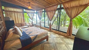 A bedroom with a bed, curtains, a desk, and a view of greenery.