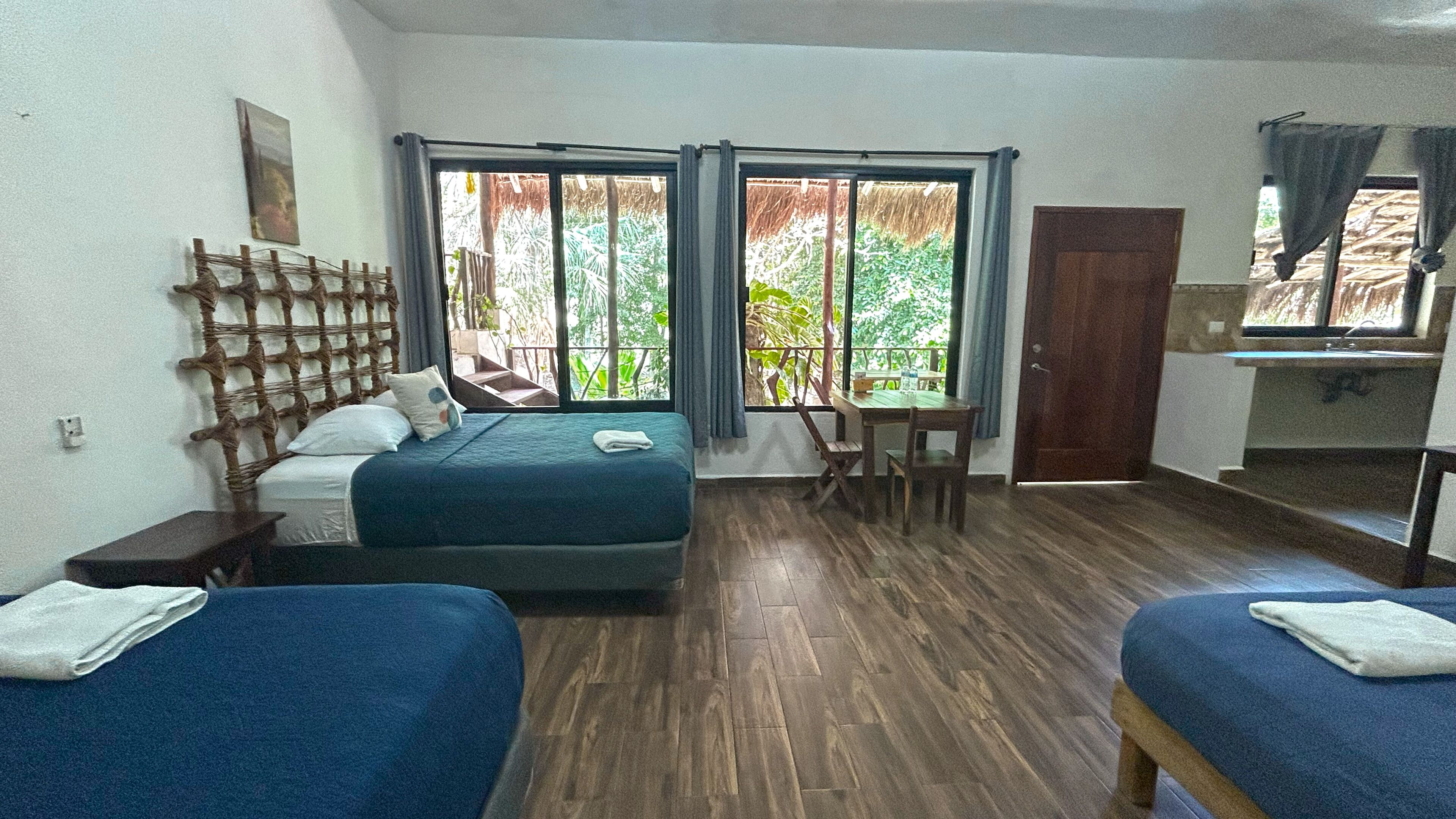 A room with a bed, a desk, and a window with a view of greenery.
