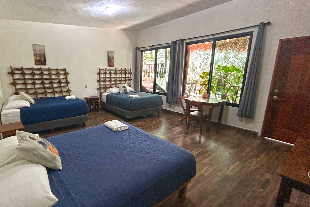 Habitación de hotel con dos camas, una mesita y una ventana con vistas a zonas verdes.