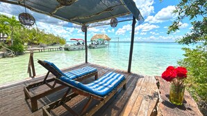 Een houten terras met twee loungestoelen, een rieten parasol en uitzicht op zee.