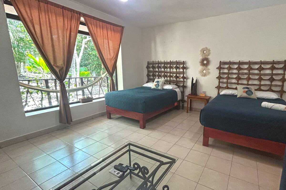 Habitación con dos camas, una ventana con cortinas, una mesita y vistas a zonas verdes.