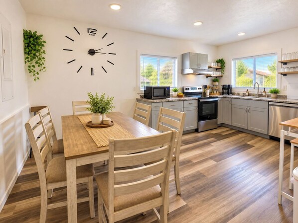 A modern kitchen with a wooden dining table, chairs, a clock, and a microwave.