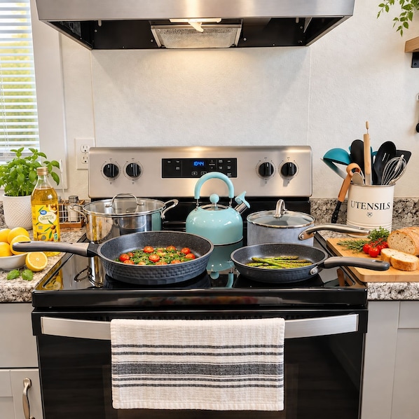 A kitchen with a stove, pots, a kettle, and a variety of cooking utensils.