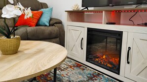 A living room with a sofa, a TV, a fireplace, and a table with a plant.
