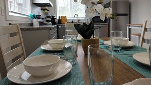 A dining table set with white plates, bowls, and clear glasses, with a woven basket containing a plant.