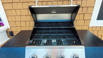 Een draagbare gasgrill met een zwarte en roestvrijstalen afwerking, voorzien van drie bedieningsknoppen en een metalen handgreep op het deksel.