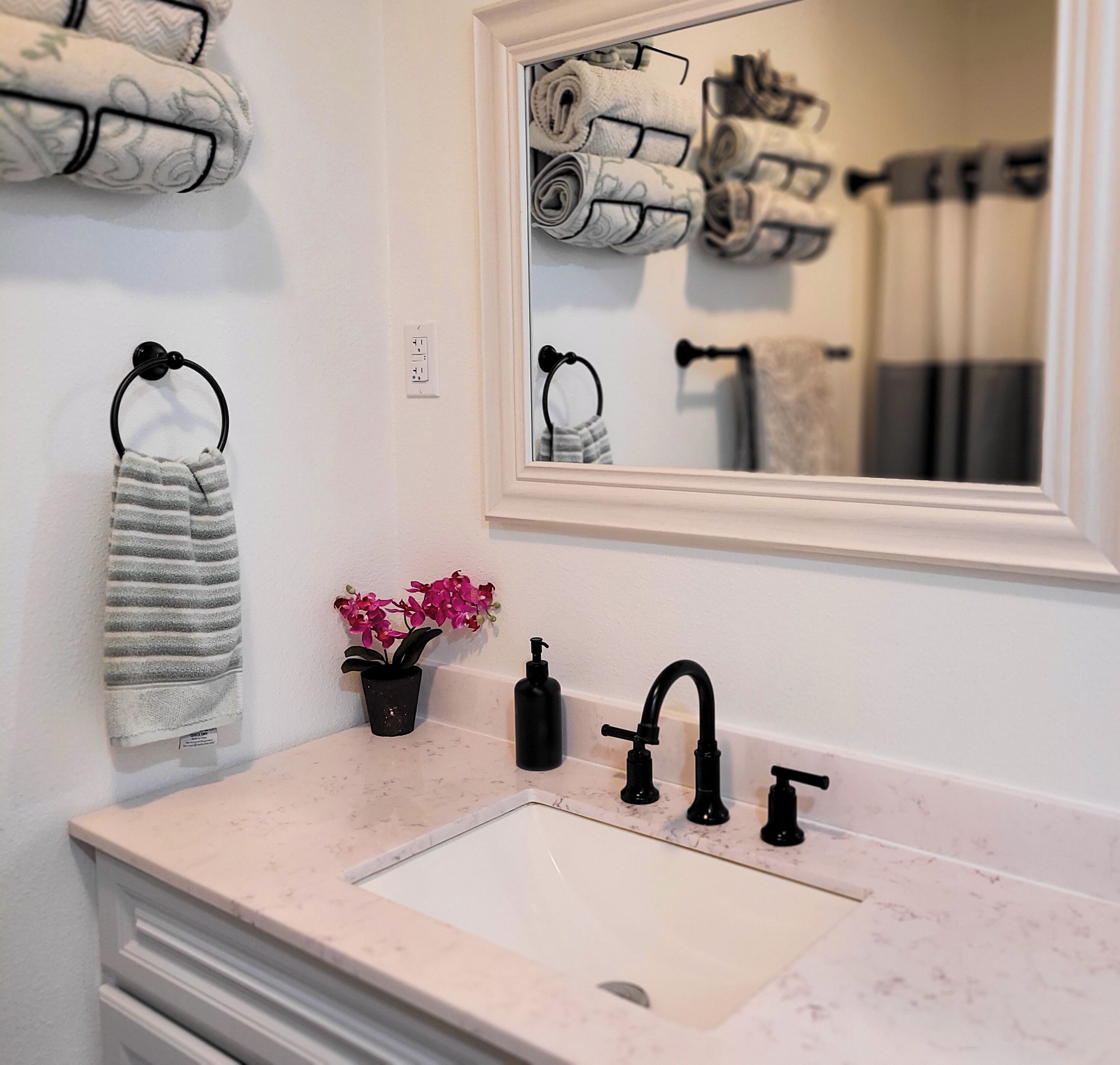 A bathroom with a white sink, black faucets, a mirror, and towels on hooks.
