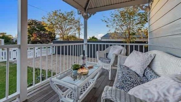 A covered porch with wicker furniture and a glass table, overlooking a yard with trees and a house.