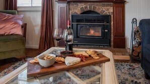 A cozy living room with a fireplace, a glass coffee table, and a wooden board with snacks and drinks.
