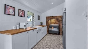 A kitchen with white cabinets, a wooden countertop, a coffee machine, and a brick wall.