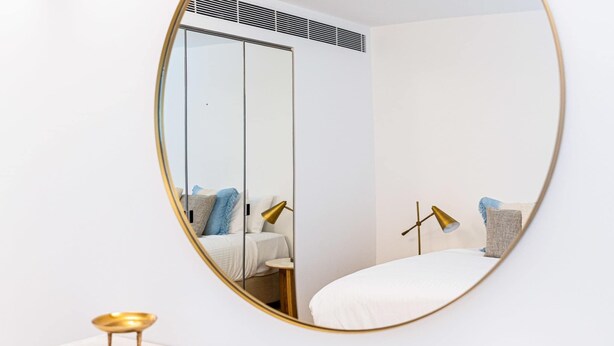 A bedroom with a bed, bedside table, lamp, and a mirror.