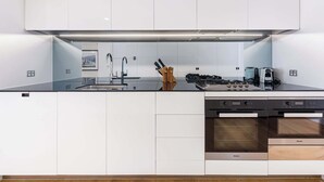A modern kitchen with white cabinetry, a stainless steel range hood, and a built-in oven.