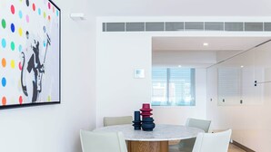 A modern dining area with a round table, white chairs, and a colorful abstract painting on the wall.