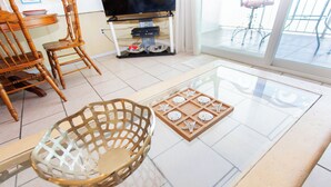 Een kamer met een glazen salontafel, houten stoelen, een houten dienblad met zeesterren en een televisie op de achtergrond.
