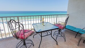 Een balkon met een tafel en stoelen, met uitzicht op een strand met parasols en mensen.