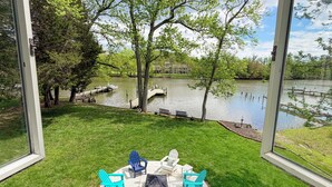 Eine Terrasse mit Gartenmöbeln, ein Betonweg und Blick auf einen See mit Bäumen und einem Steg.